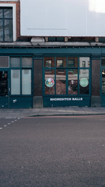 This image depicts the exterior of Shoreditch Balls, a flowershop located on a city street, with a dark storefront featuring large windows displaying signs for 'Kids' and 'Sale.' The shop name is in w